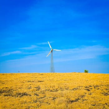 A solitary windmill stands tall on a golden, grassy field under a vibrant blue sky.