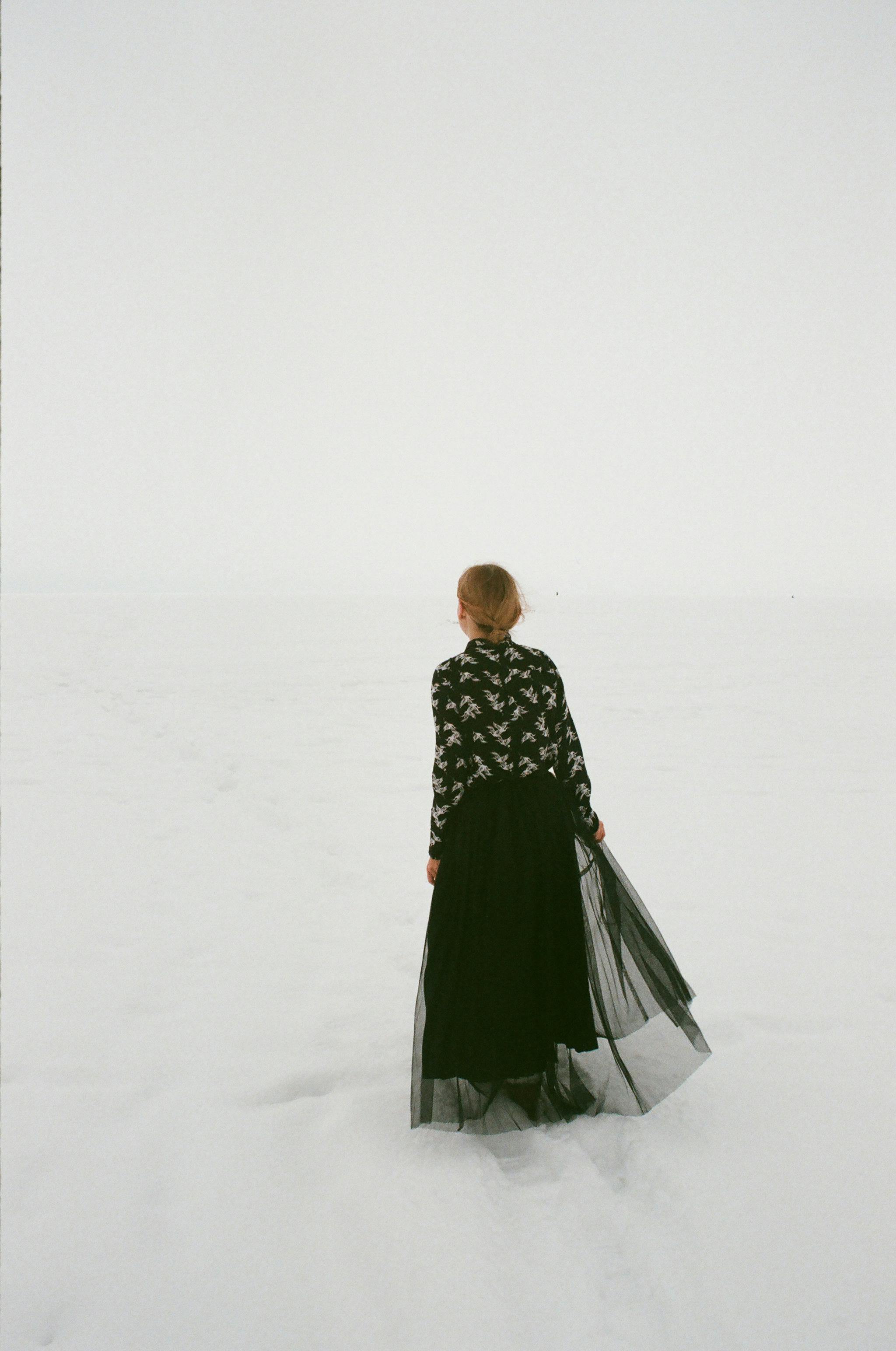 一名身穿黑色连衣裙的女子，站在广阔的雪景中，令人感到孤独