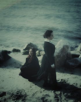 Two women in black attire captured in a dreamy seaside portrait with a mystical atmosphere.