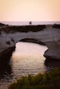 日落时分，一对夫妇在海边走过天然石拱门的宁静场景