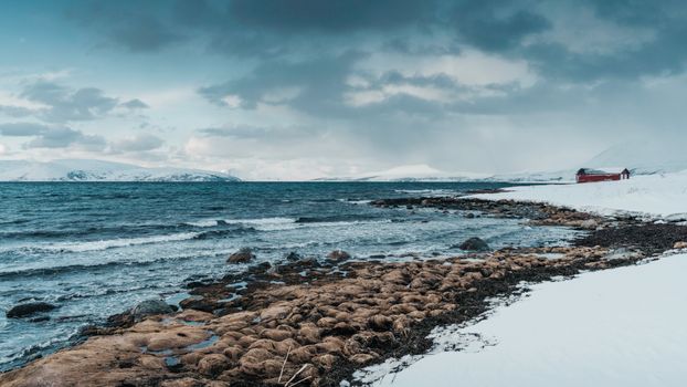 A serene snowy coastal scene with a red cabin and vast ocean view, evoking a tranquil winter atmosphere.
