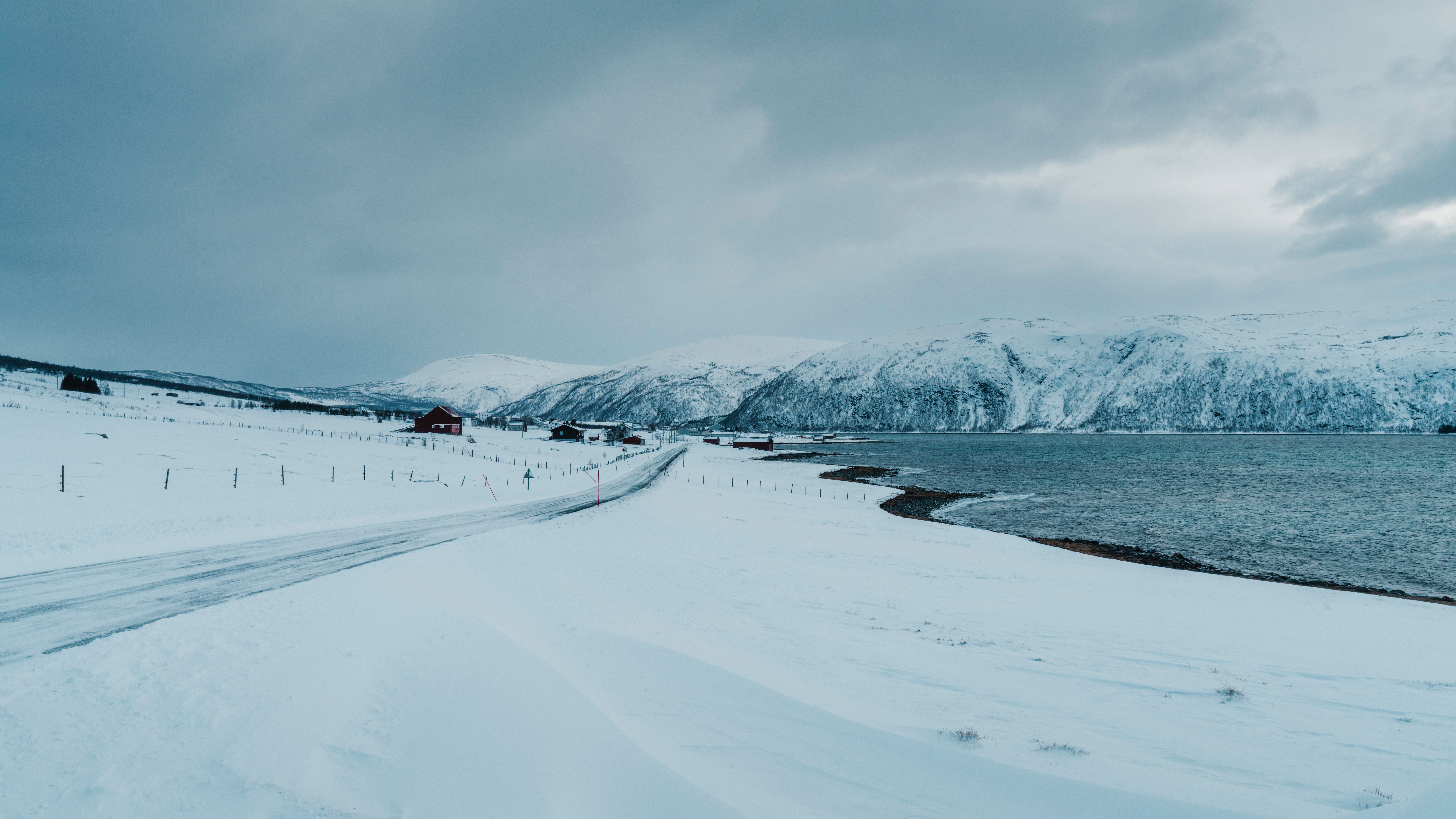 A serene winter landscape featuring snow-covered mountains and a winding road by a frozen lake.