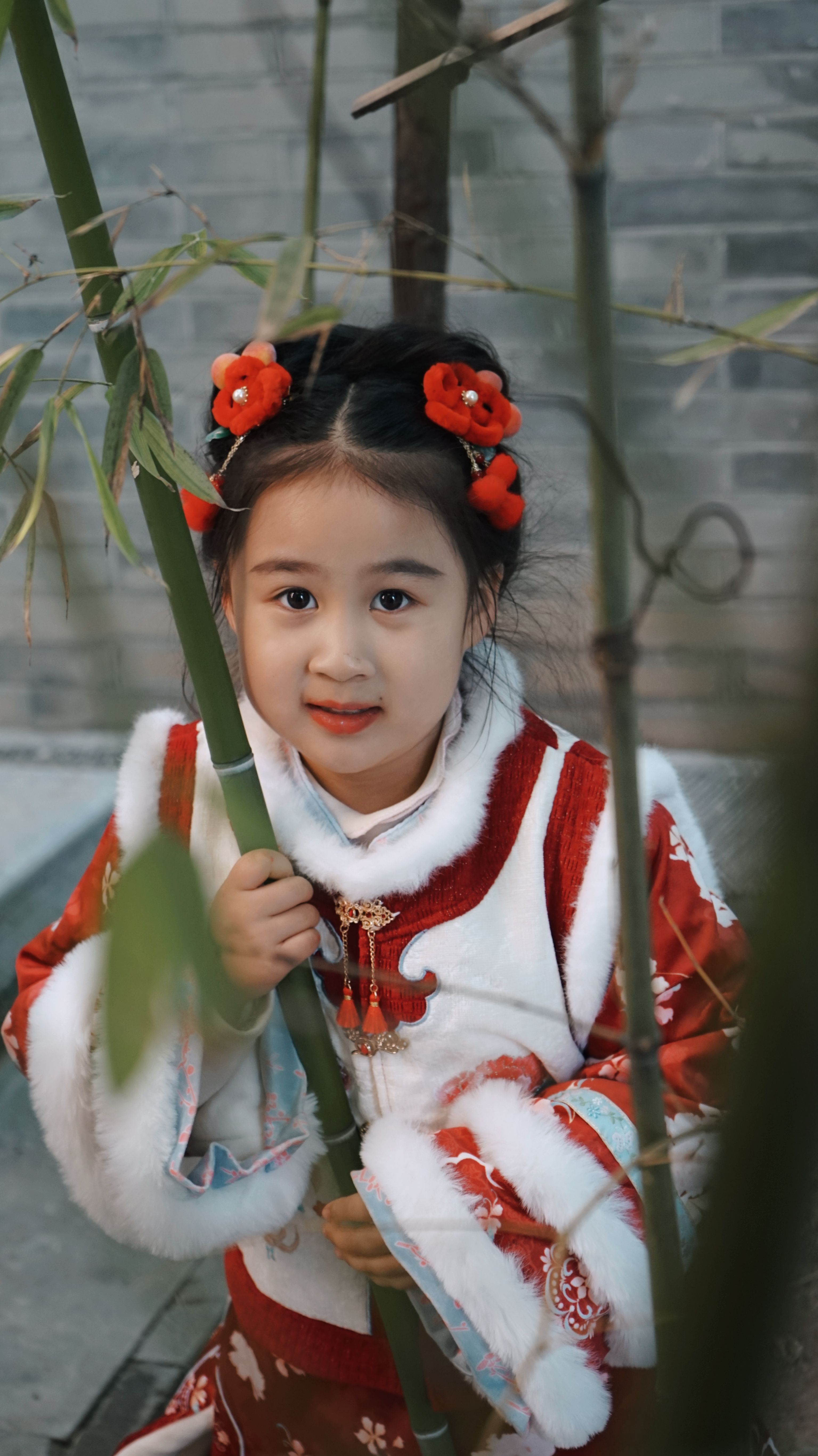 Cute little girl in traditional red and white outfit holding bamboo, featuring festive decorations.