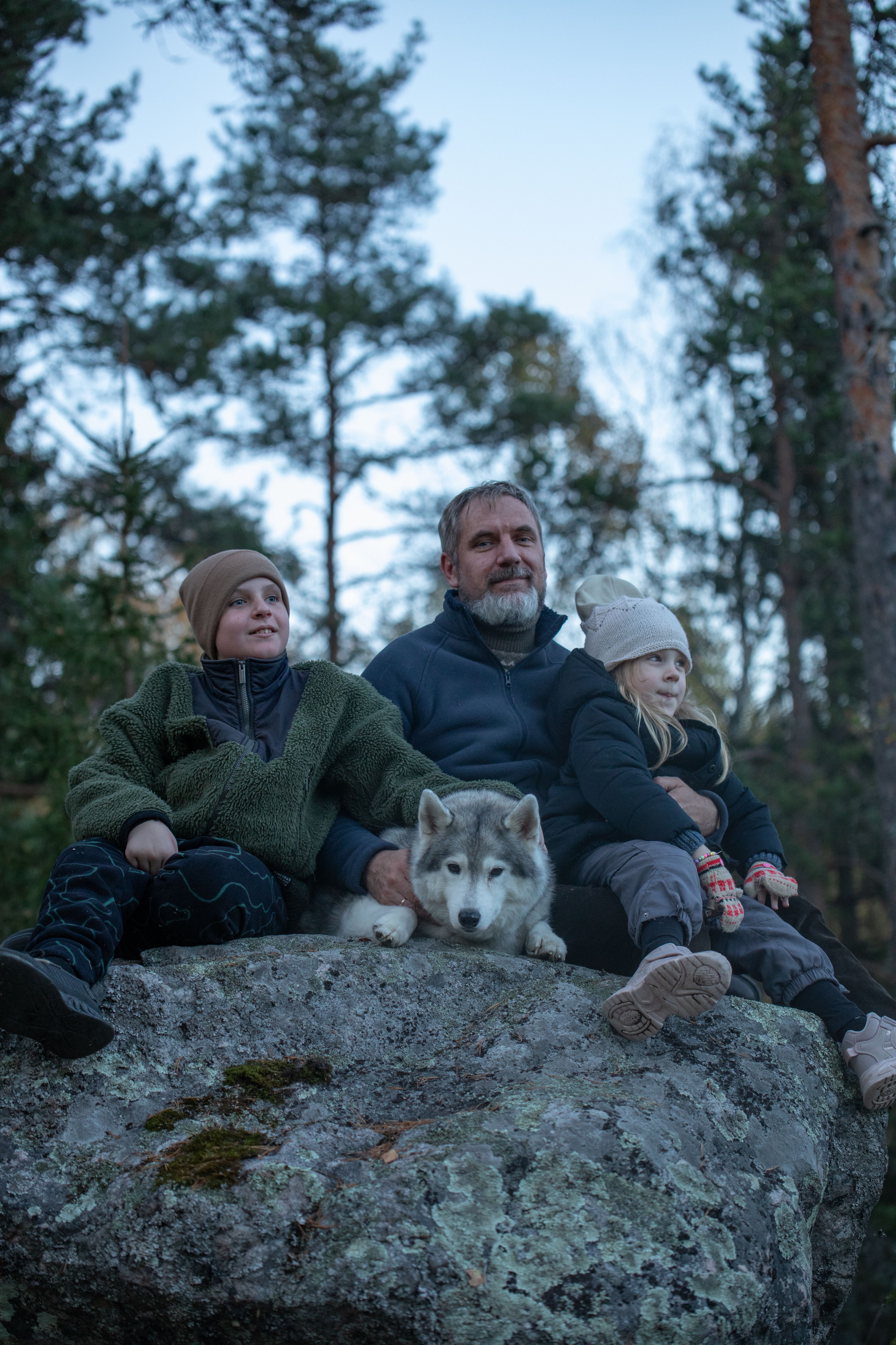 Father, two children, and husky enjoying nature on a large rock.