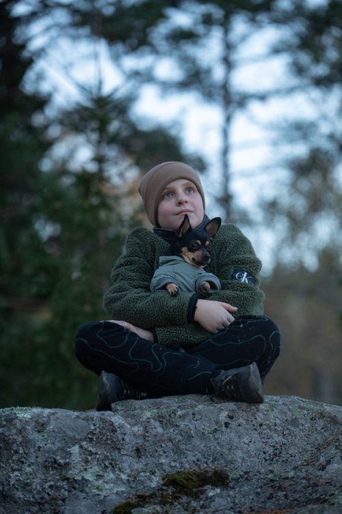 Free A young child sitting outdoors holding a small dog, showcasing companionship and nature. Stock Photo