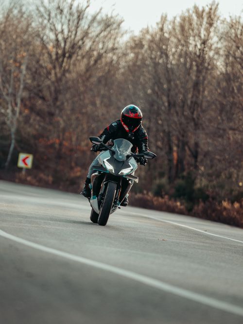 Free A motorcyclist with a helmet rides down a curvy road surrounded by autumn trees. Stock Photo