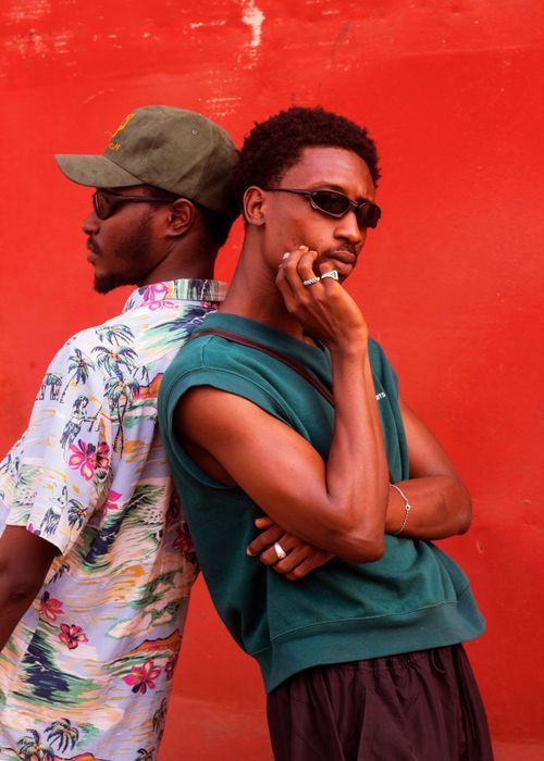 Free Two fashionable men in sunglasses pose against a vibrant red wall, showcasing street style. Stock Photo