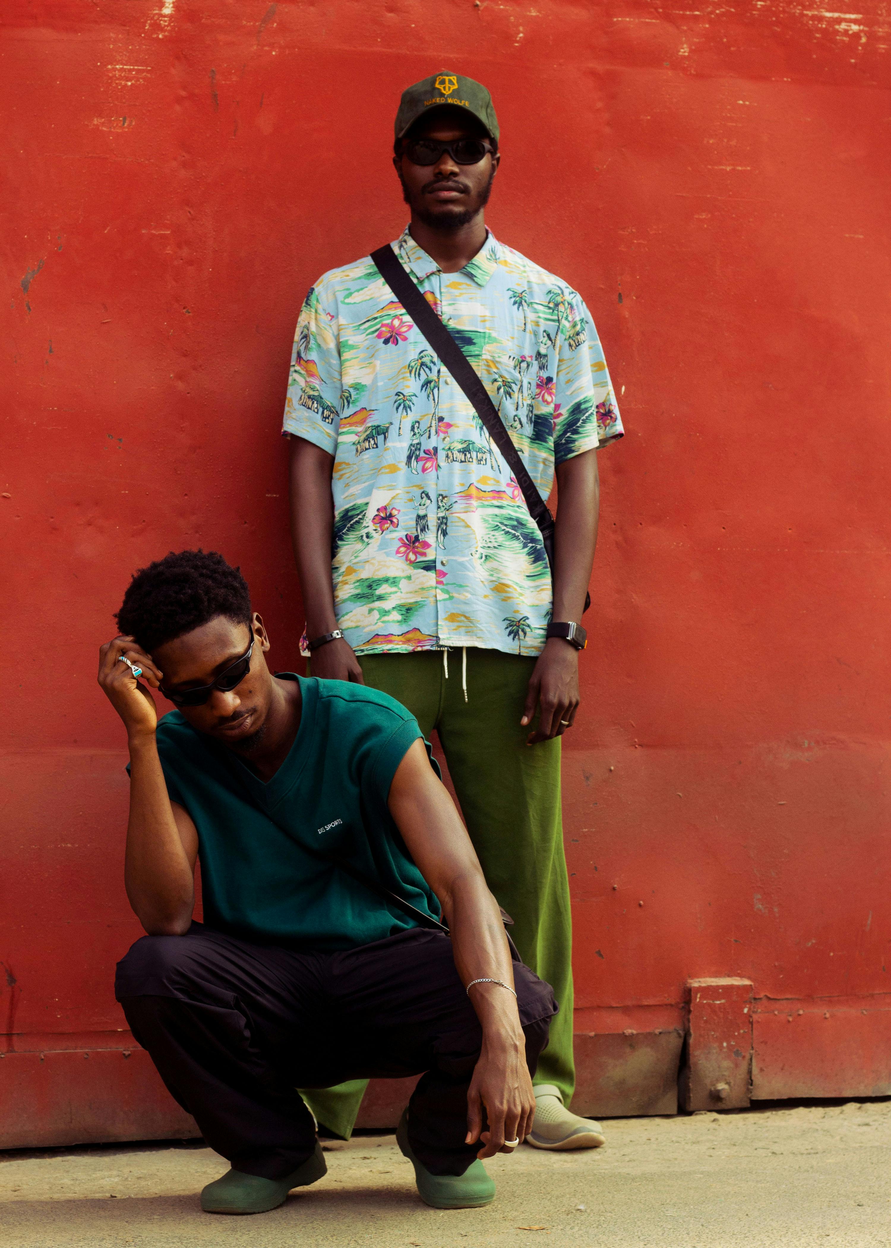 Stylish African men posing in street fashion against a red wall.
