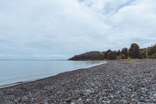 Free Tranquil pebble-strewn lakeshore with cloudy sky at Las Cascadas, Chile. Stock Photo