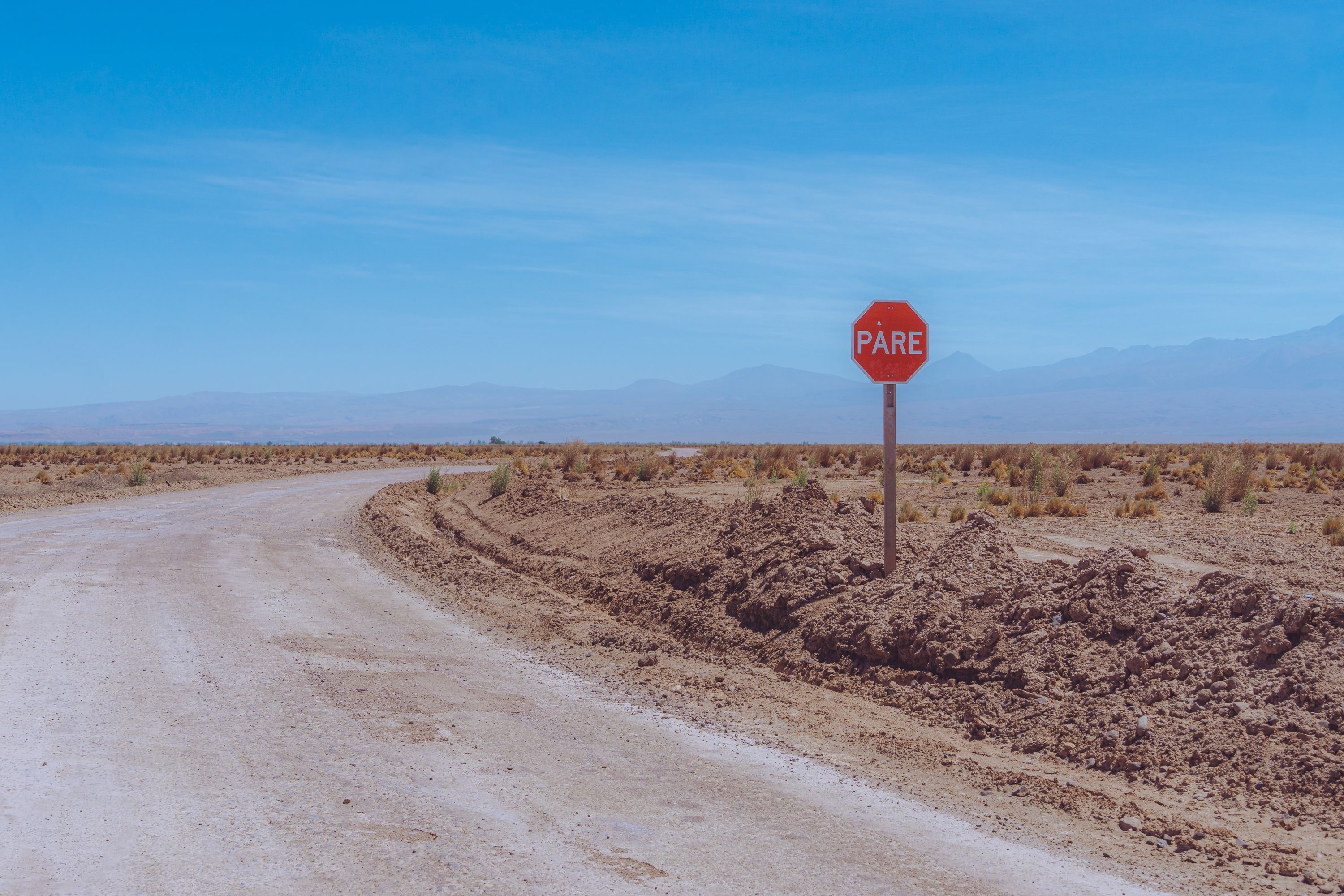 A winding dirt road alongside a 'PARE' stop sign in the Atacama Desert, Antofagasta, Chile.