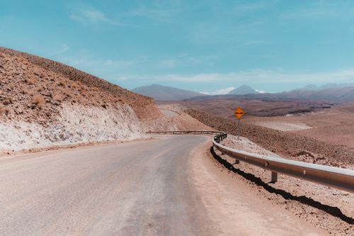 Free A winding deserted road in the Antofagasta desert, showcasing the barren landscape under a clear blue sky. Stock Photo