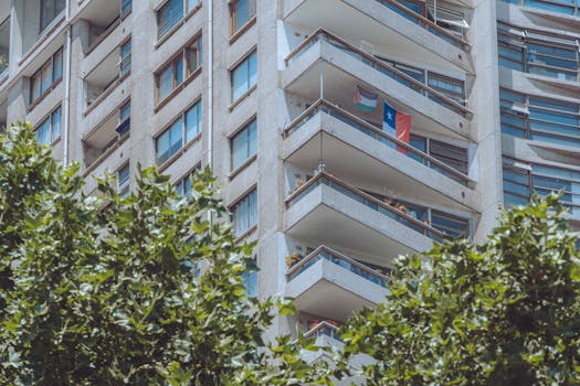 Modern apartment building in Santiago with a Chilean flag on the balcony, surrounded by greenery.
