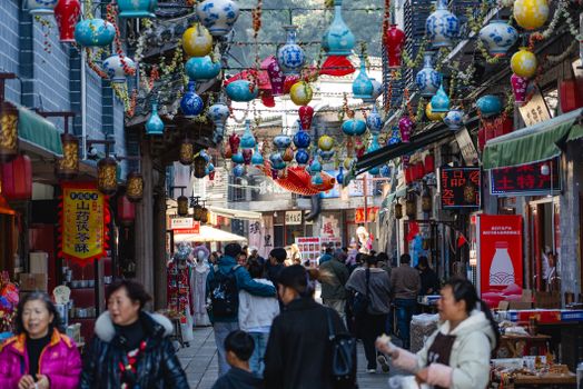 A bustling outdoor market filled with colorful lanterns and people shopping on a sunny day.
