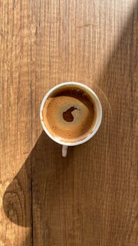 Top-down shot of coffee cup casting shadow on textured wood surface.