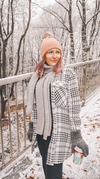 Woman in winter clothing holding a hot drink on a snowy day outdoors.