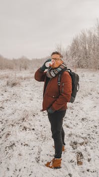 Man enjoying a hot drink during a snowy winter walk in a scenic landscape.