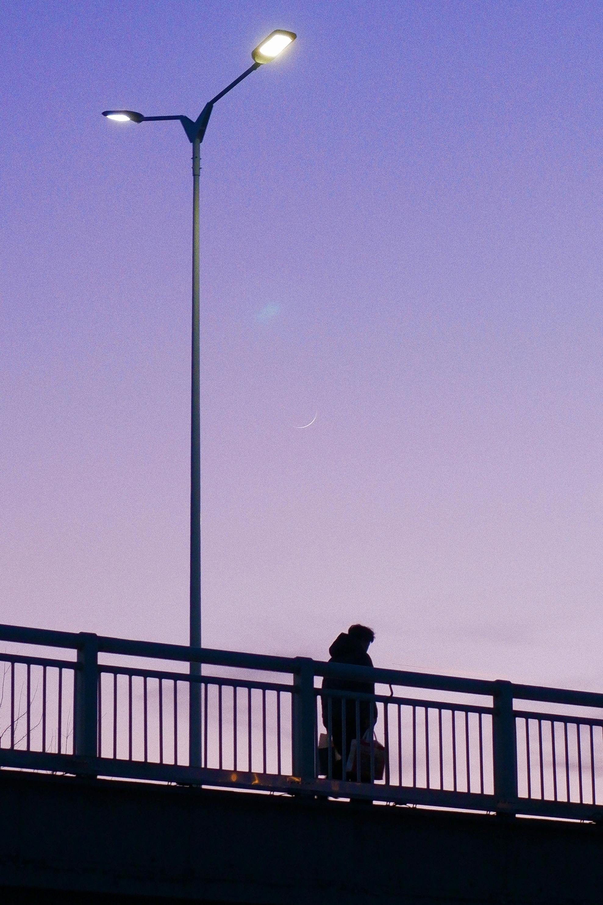 A solitary figure silhouetted against a twilight sky on a city bridge, evoking solitude.
