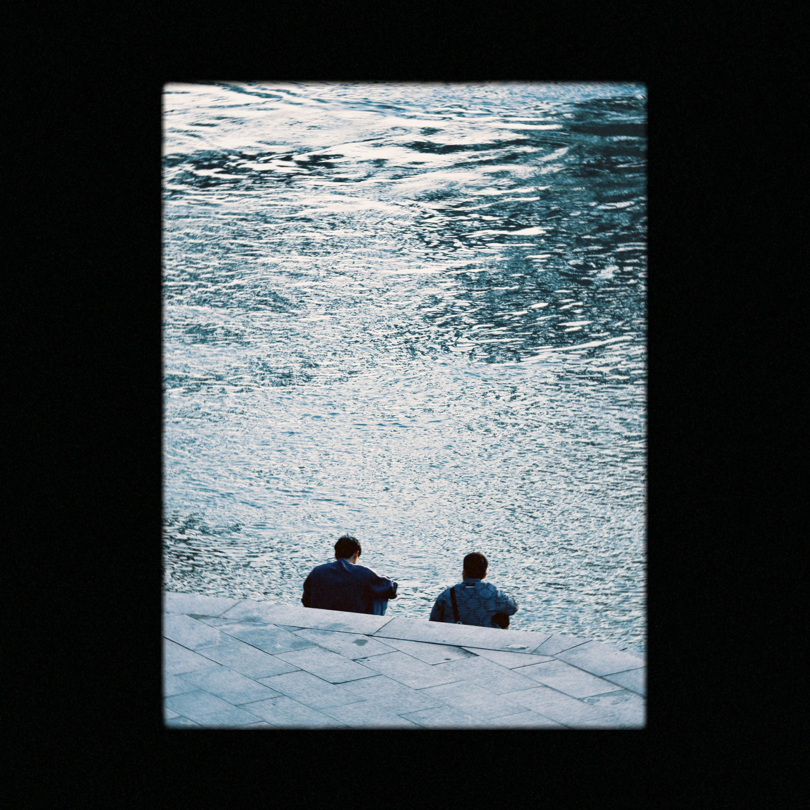 Serene scene of two people sitting by a river, enjoying the tranquility.