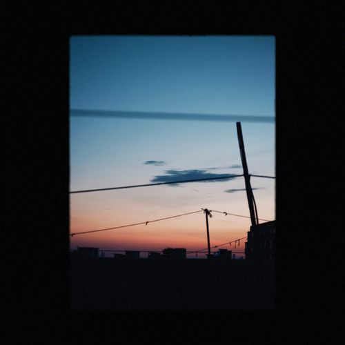 Free Silhouette of city skyline against a vibrant sunset through power lines. Stock Photo
