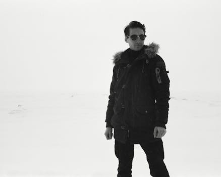 A man in winter clothing stands alone in a vast snowy landscape, exuding a sense of solitude.