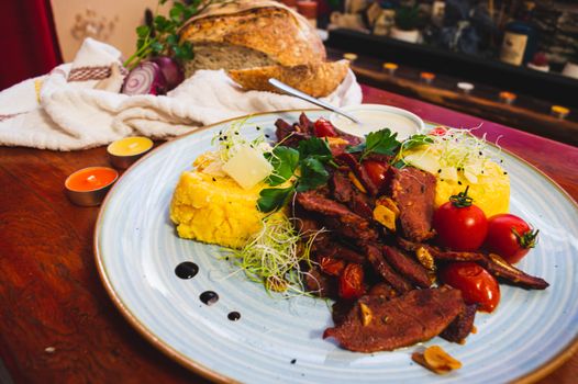 Savor a traditional Romanian meal featuring juicy beef, polenta, and fresh vegetables, perfect for a culinary adventure.