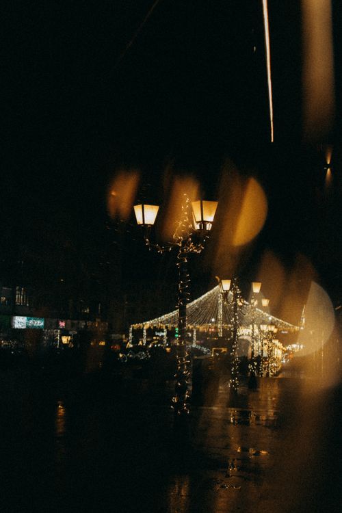 Free Charming street lights illuminate a city street with a warm bokeh effect, perfect for seasonal or moody themes. Stock Photo