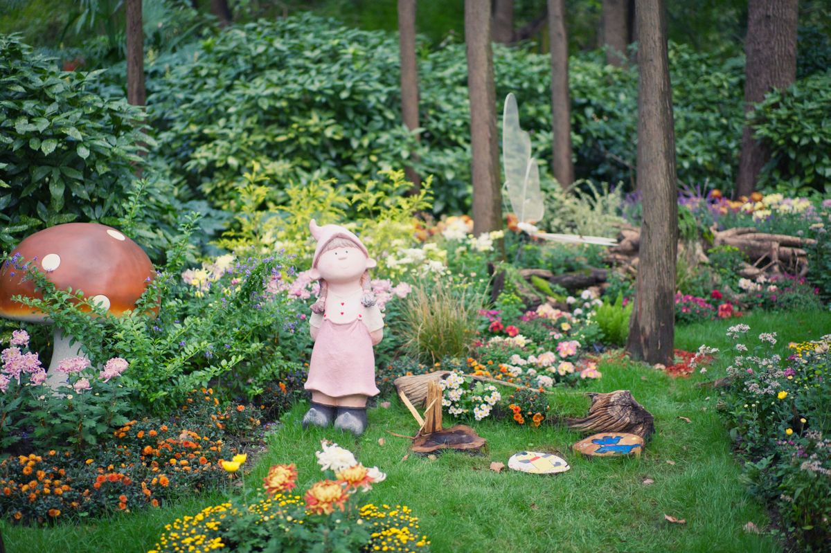 Charming garden scene with a fairy statue, mushroom, and colorful flowers. Stock Photo.