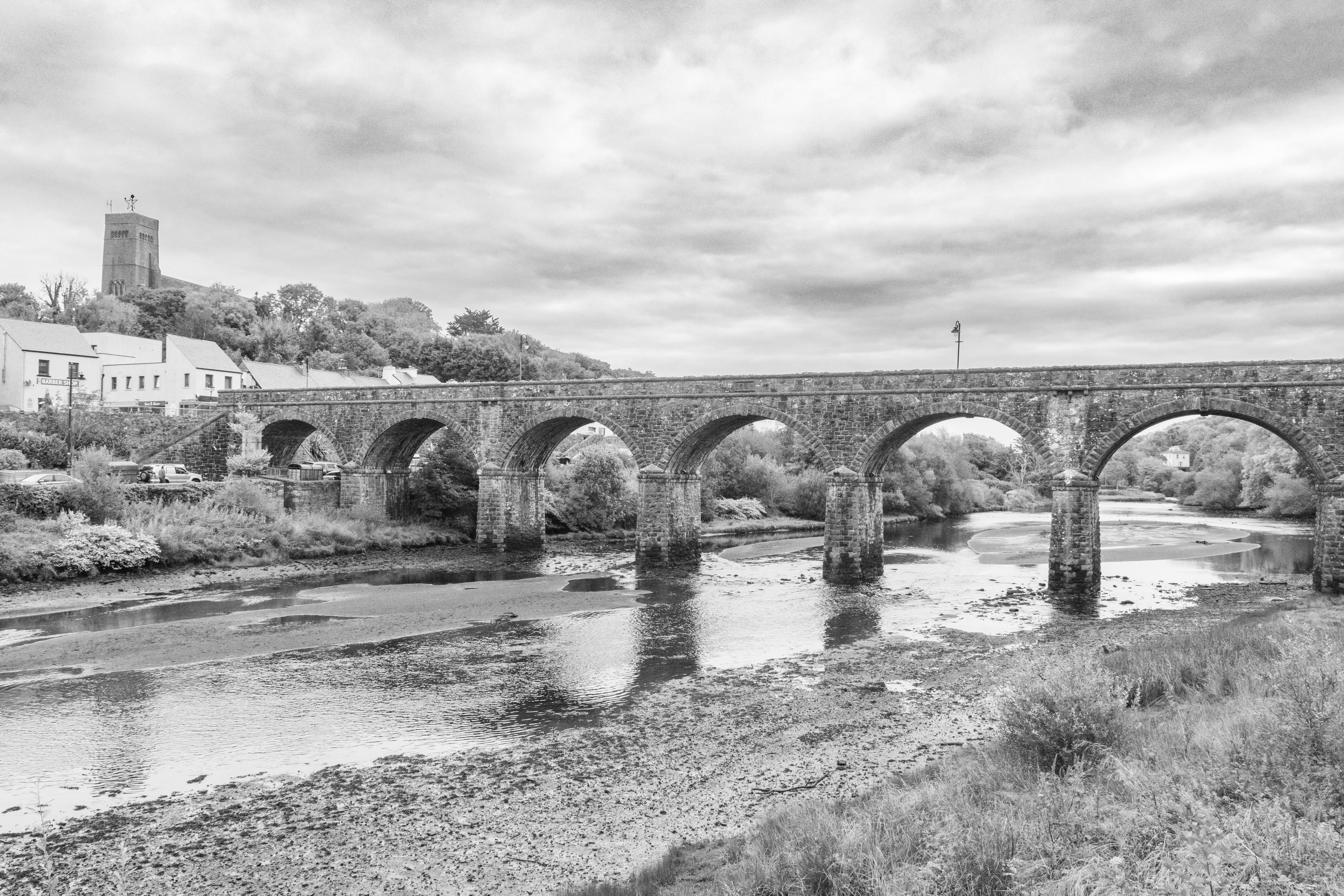 Black and white photo of a historic stone bridge over a river in Newport, County Mayo.