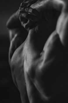 Moody black and white image capturing the muscular back of a man in an artistic pose.