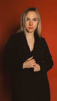 A professional woman stands confidently in a black suit against a vibrant orange background.