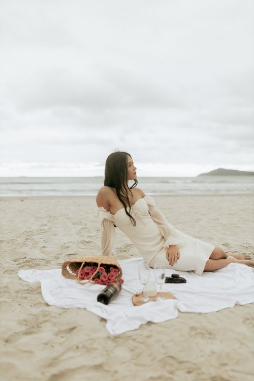 Free Woman enjoying a beach picnic with wine and grapes, embracing coastal relaxation. Stock Photo