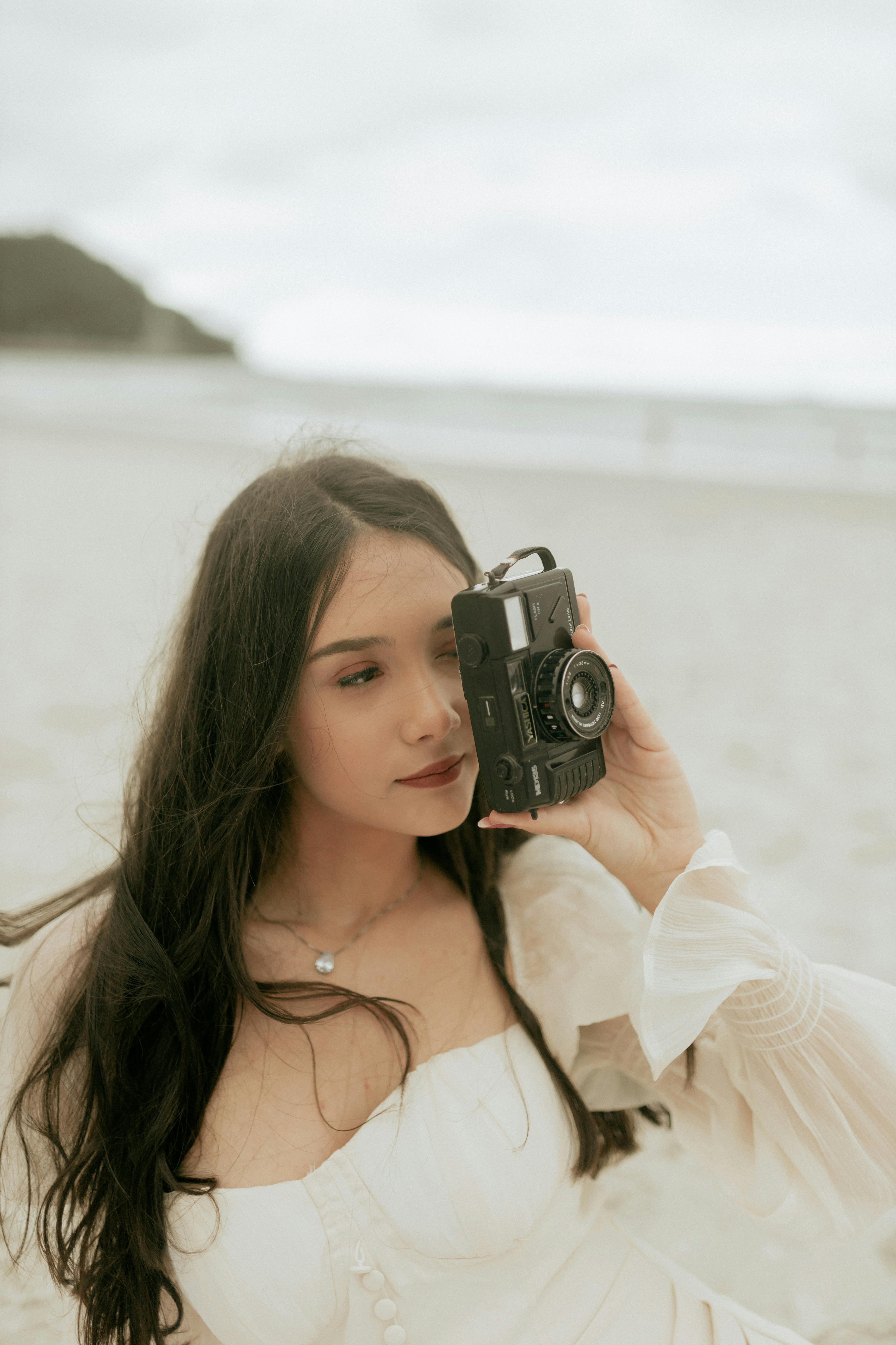 A young woman using a vintage camera at the beach, capturing moments.