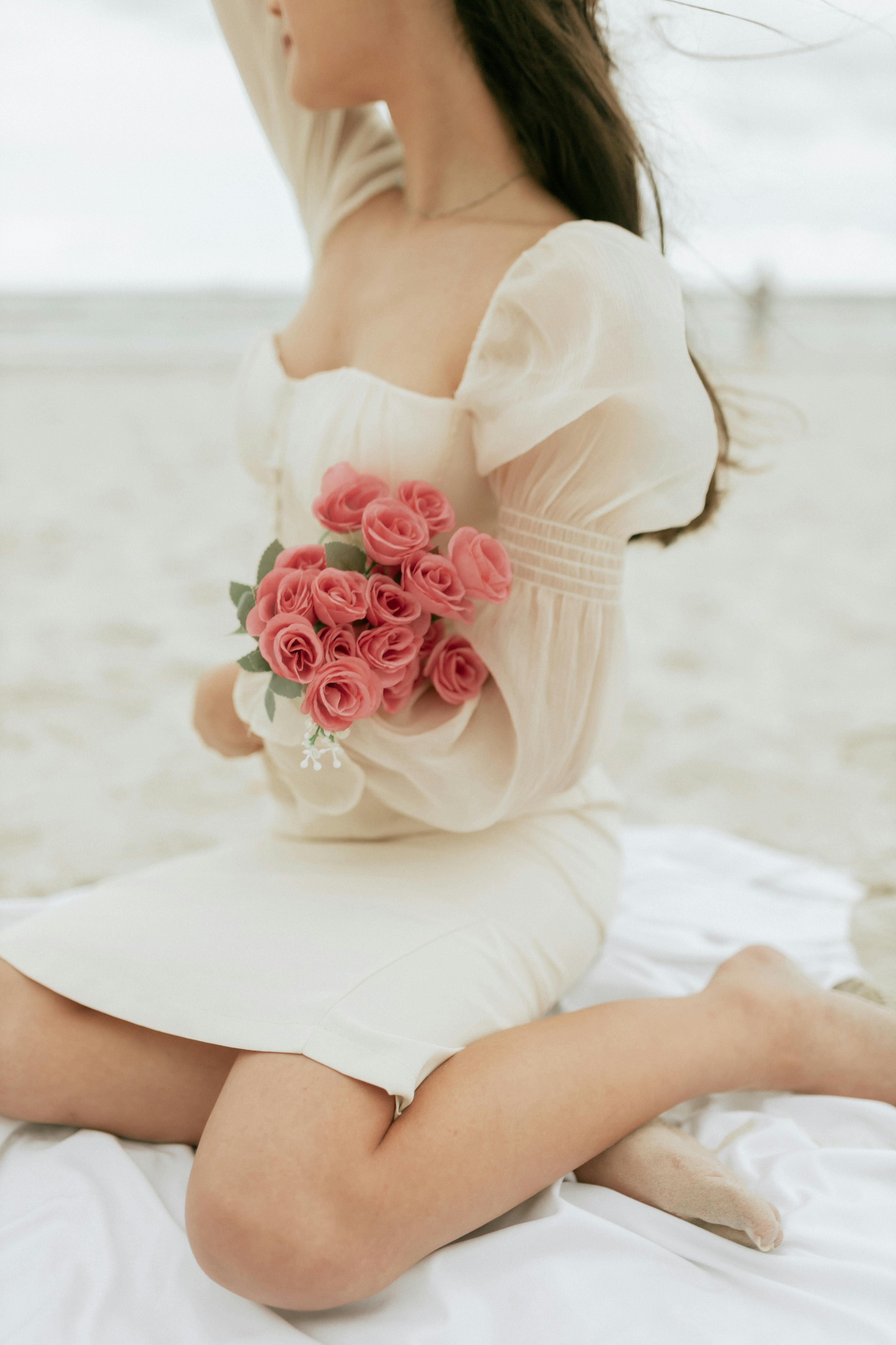 A serene scene of a woman holding pink roses on a sandy beach, capturing elegance and tranquility.
