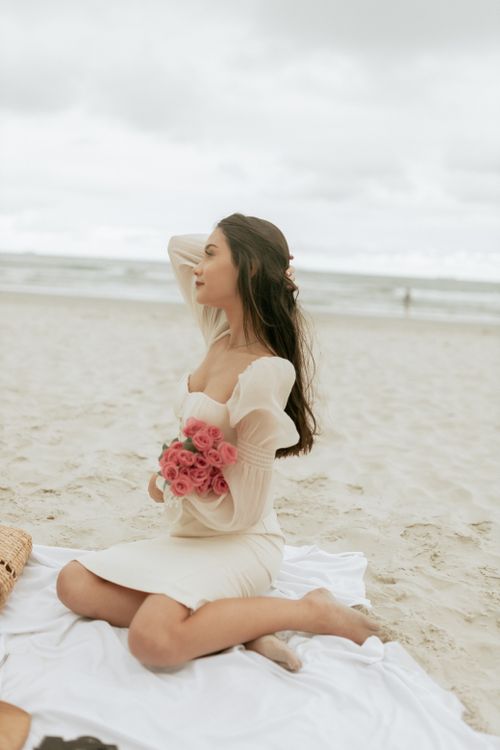 Free Elegant woman holding roses on a serene beach, enjoying the peaceful seaside ambiance. Stock Photo