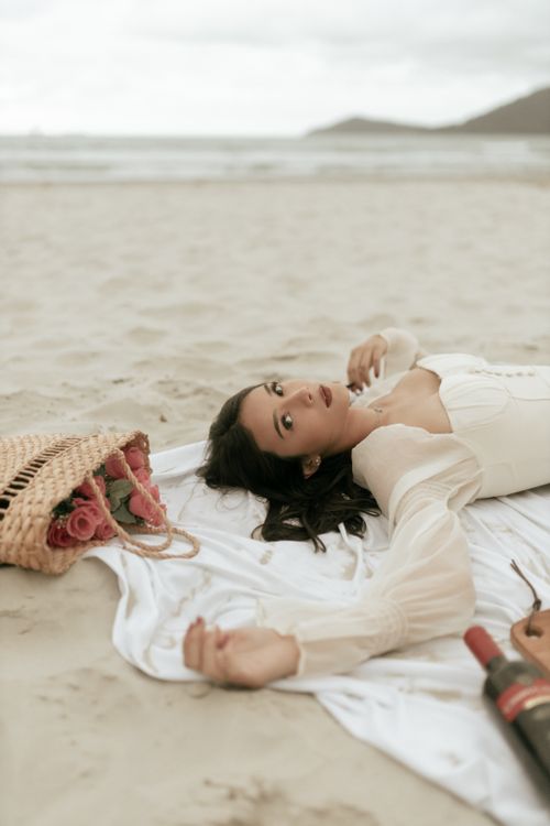 Free Woman in white dress enjoying a serene beach picnic with roses and wine. Stock Photo