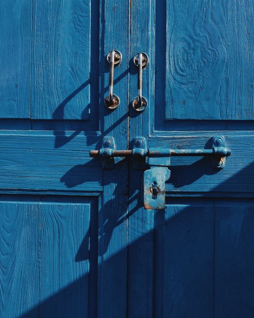 Close-up of a blue wooden door with rustic metal handles and lock.