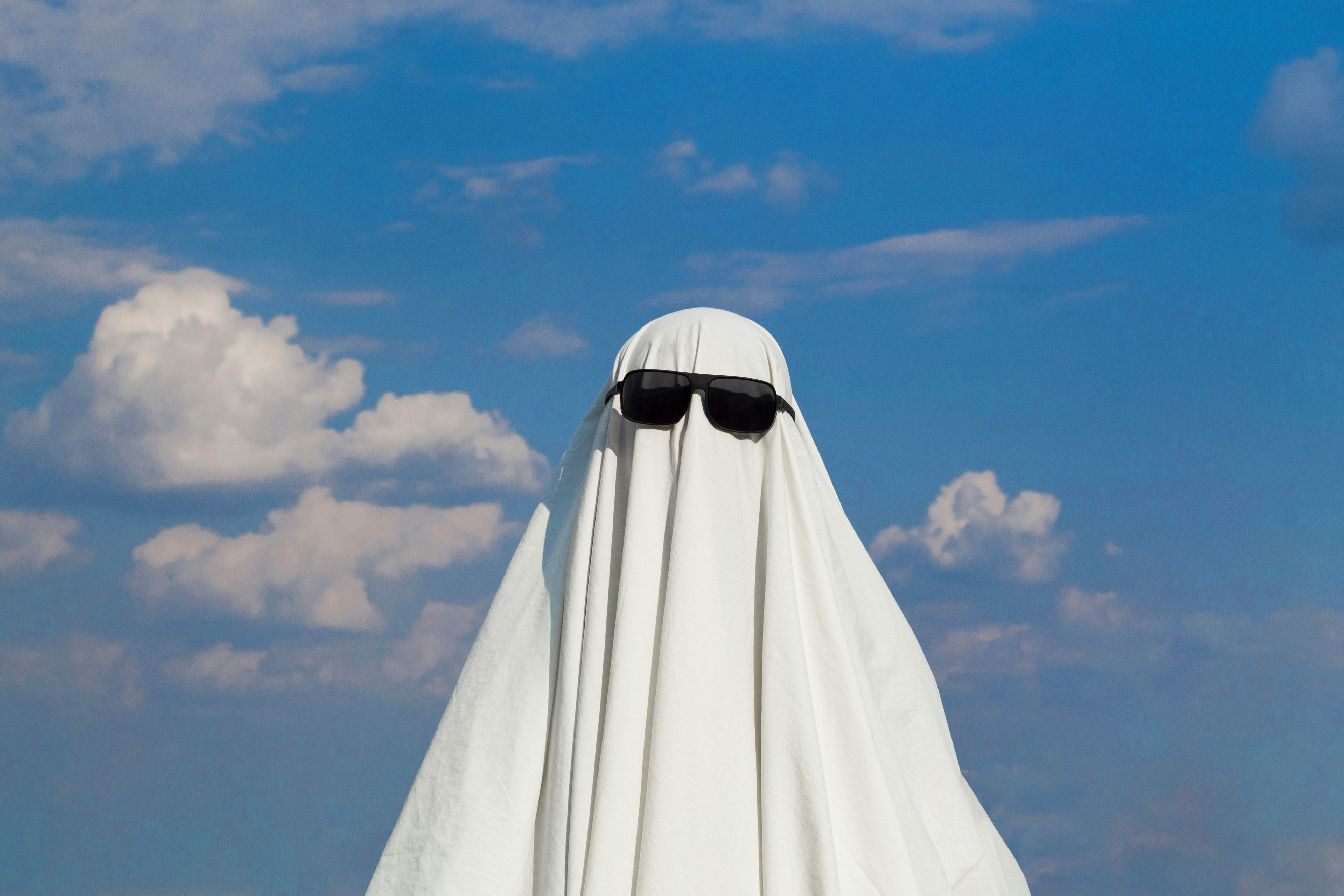 A humorous image of a person in a ghost costume with sunglasses, set against a blue sky.