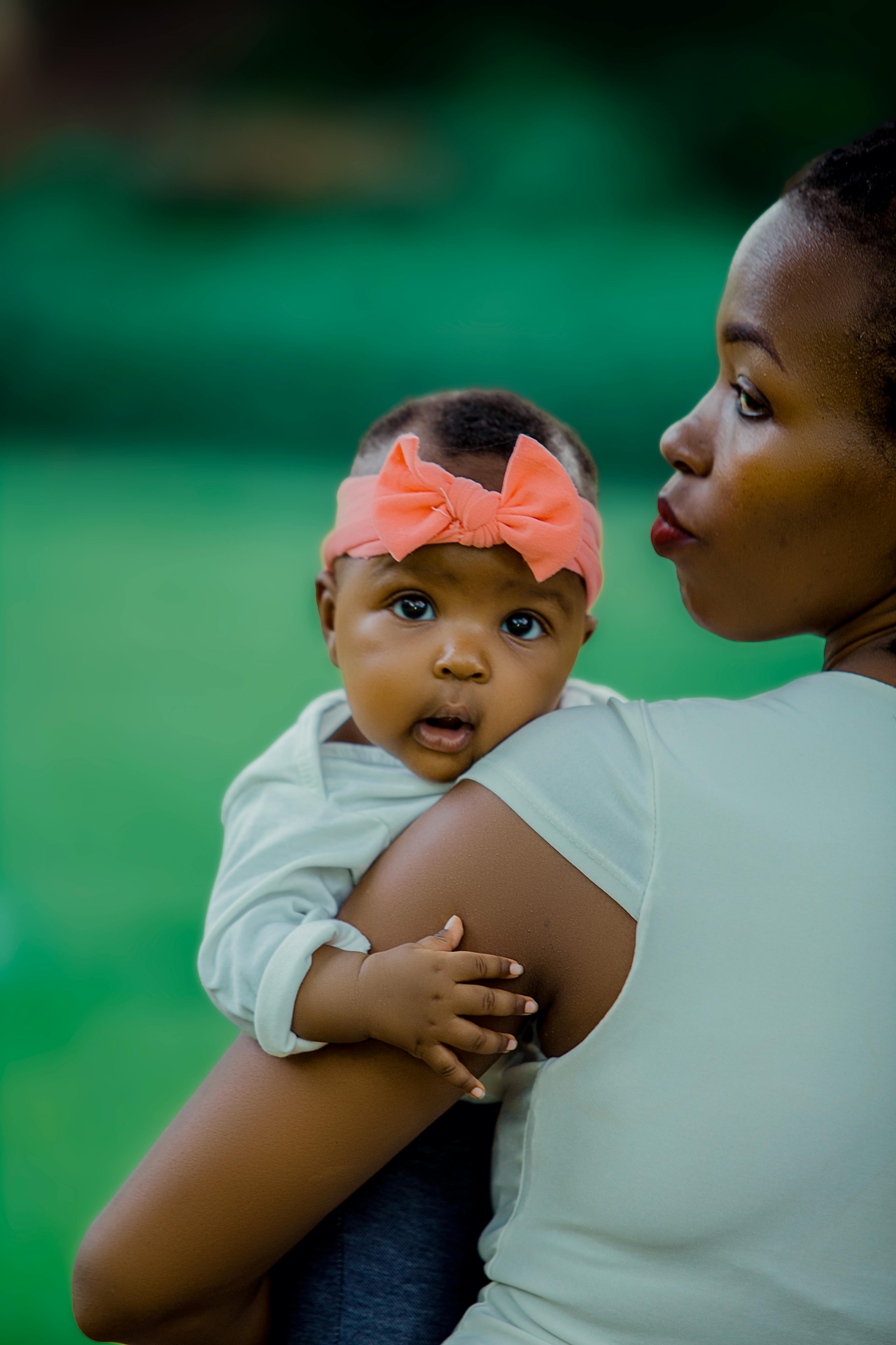 mother holding baby with pink bow outdoors