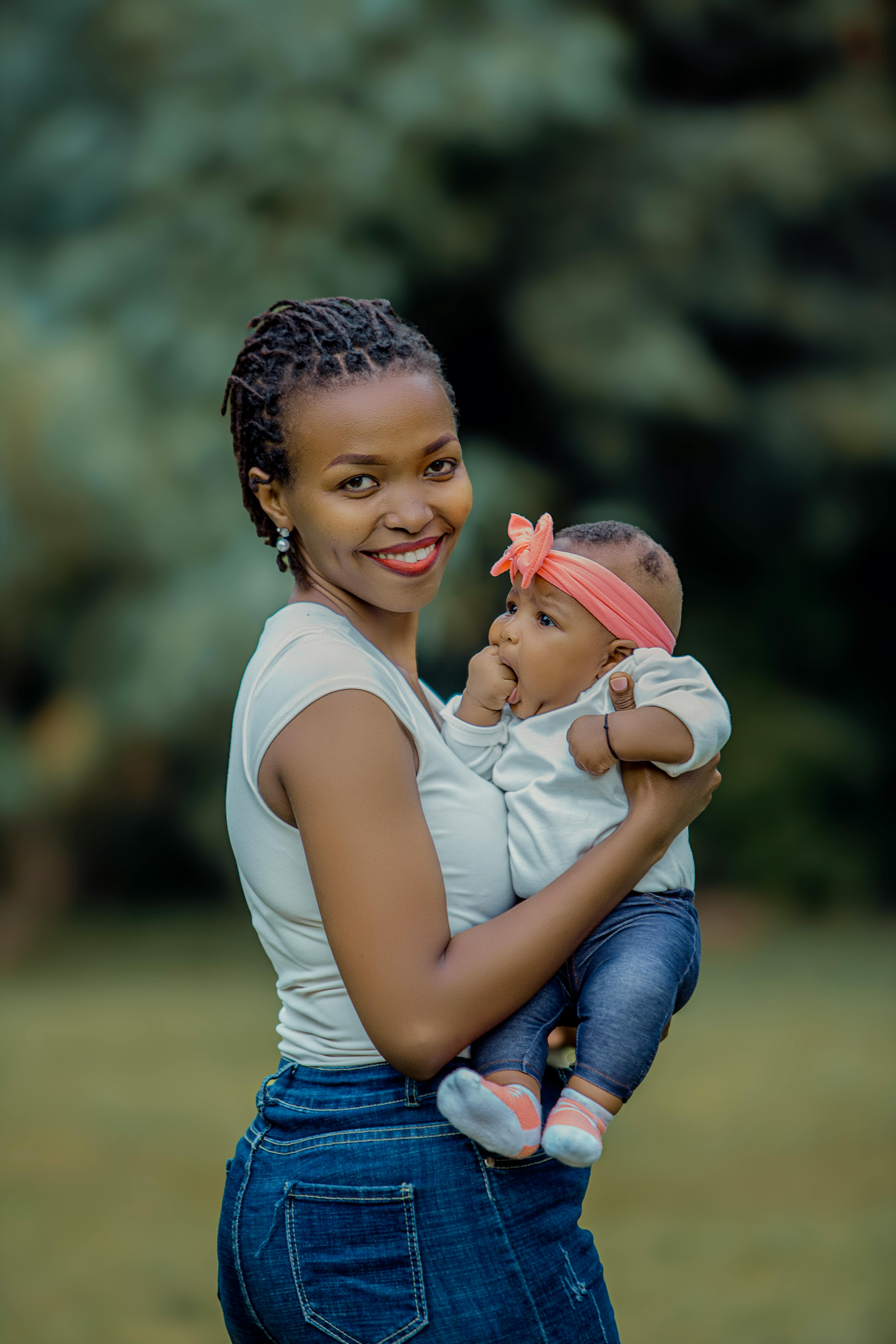 Smiling mother lovingly holding her baby outdoors in a lush green park setting.