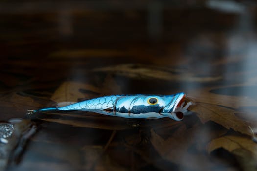 Close-up of a realistic fish-shaped lure floating in a natural water environment with leaves.