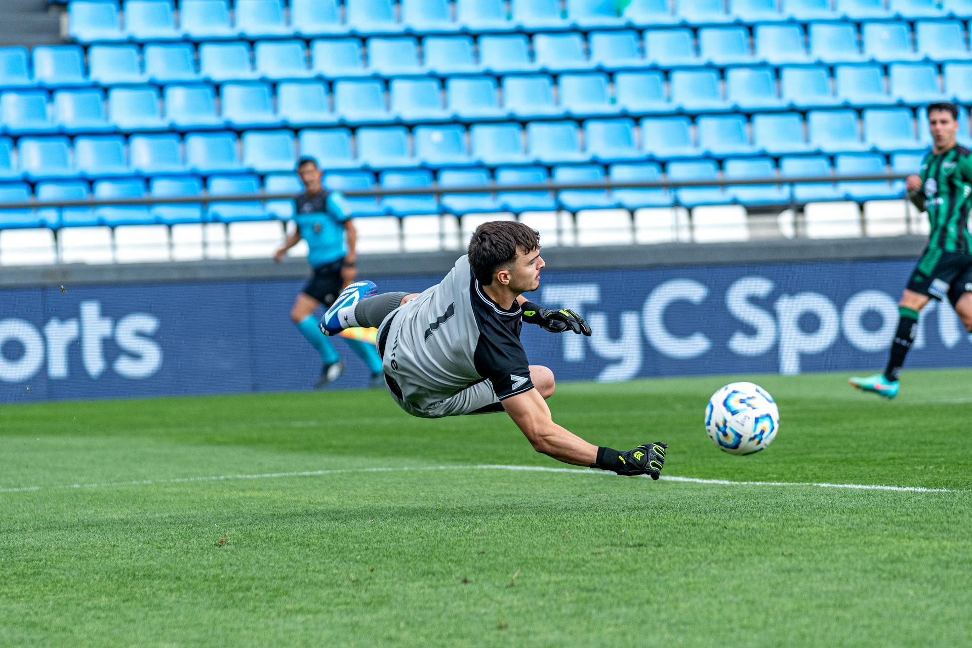 Goalkeeper dives to make an incredible save during a soccer match on a green field.