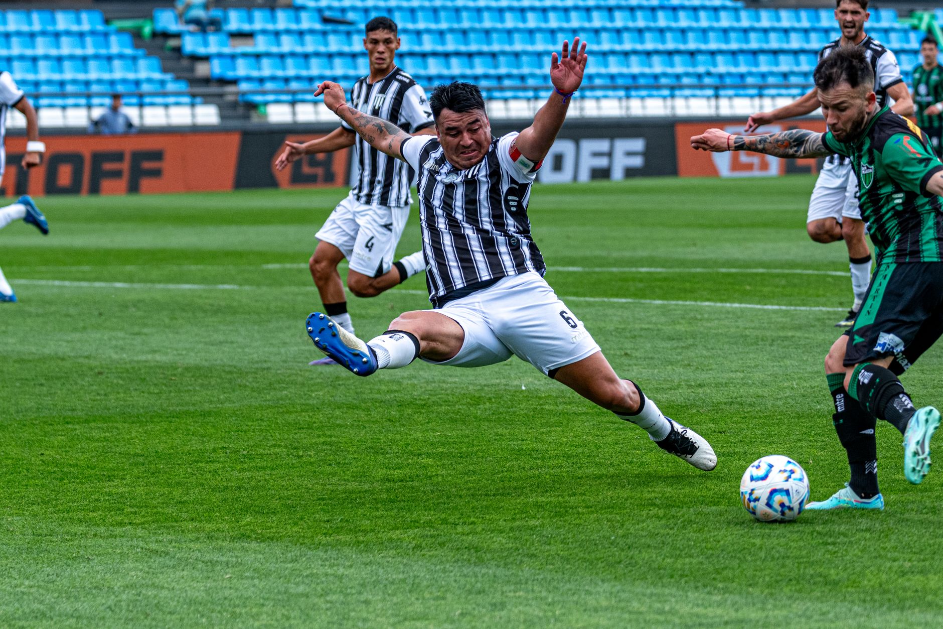 striker shooting toward a marked far-post target while a goalkeeper dives across a wet training pitch