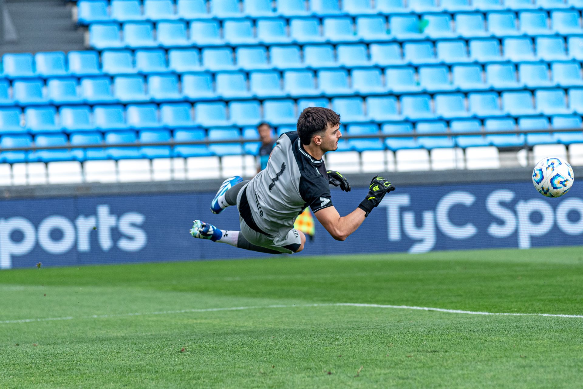 Dynamic shot of a goalkeeper diving to save a ball during a football match in an empty stadium.