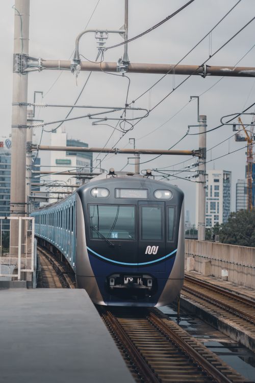 Free A sleek electric train on raised tracks amidst Jakarta's urban backdrop during the day. Stock Photo