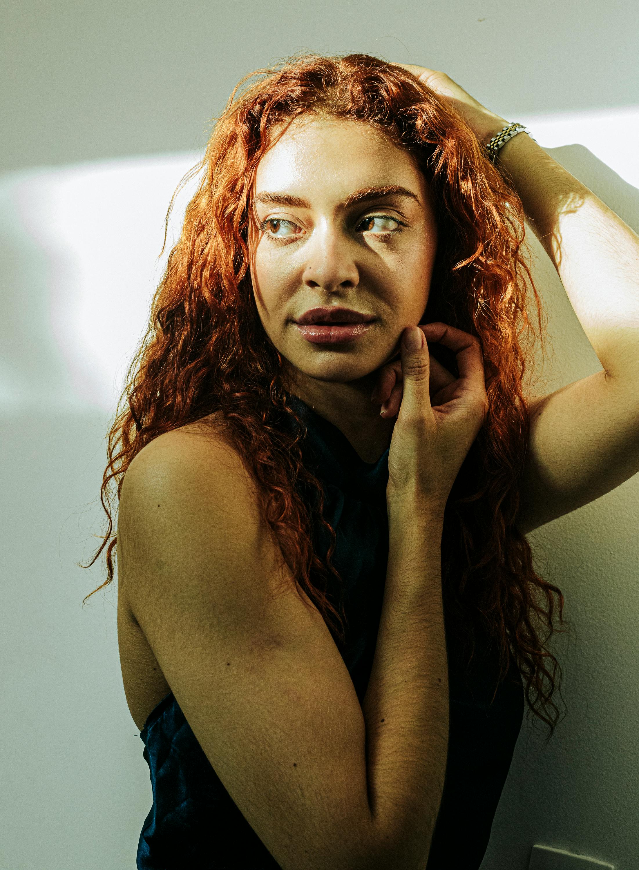 Artistic portrait of a woman with curly red hair looking thoughtfully in natural light.