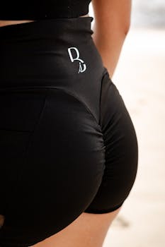 A close-up view of a person wearing black athletic shorts on a sandy beach.