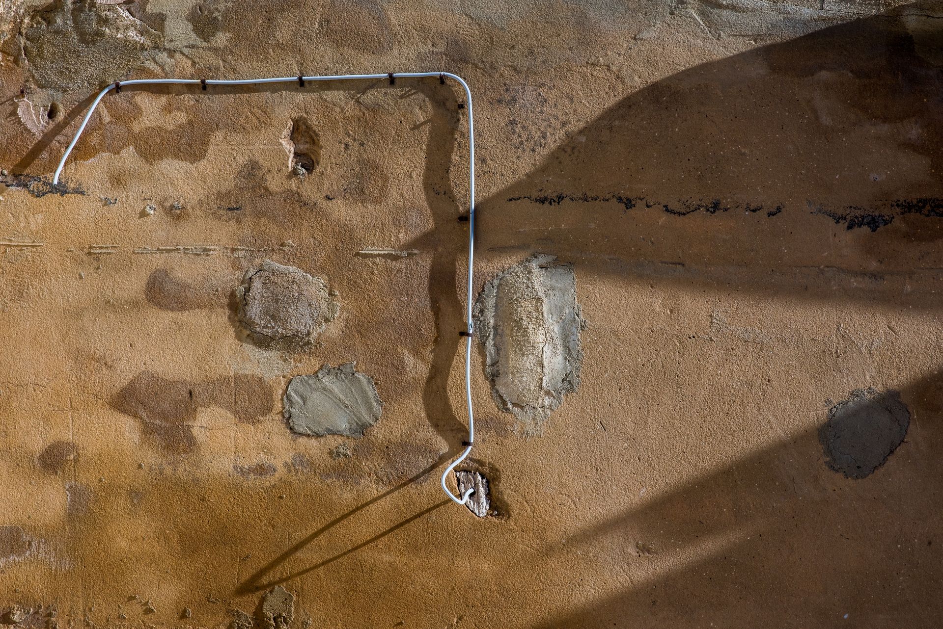 An aged wall surface with exposed wiring and shadows creates a rustic, textured view.