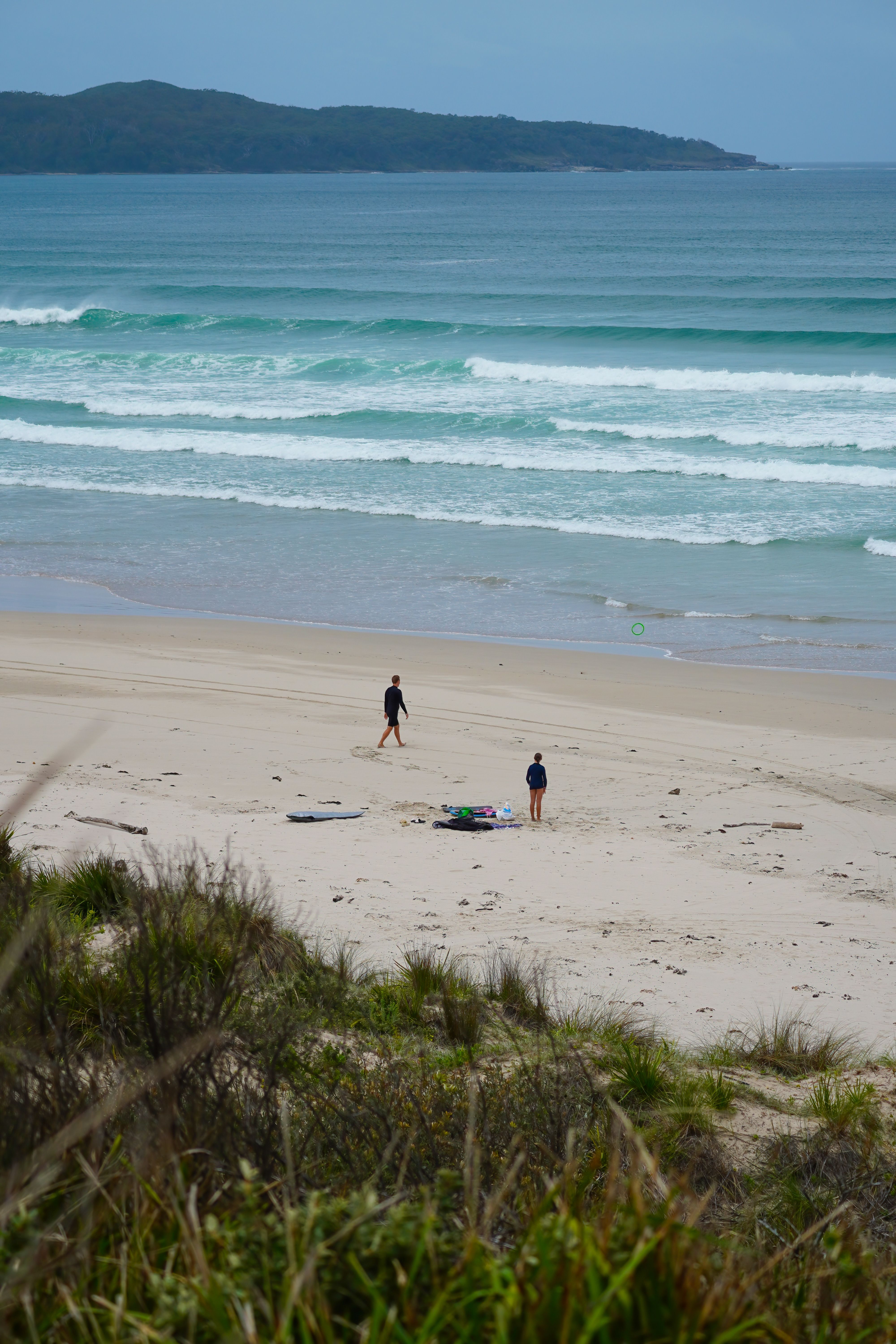 Tranquil beach with two surfers preparing on a cloudy day.