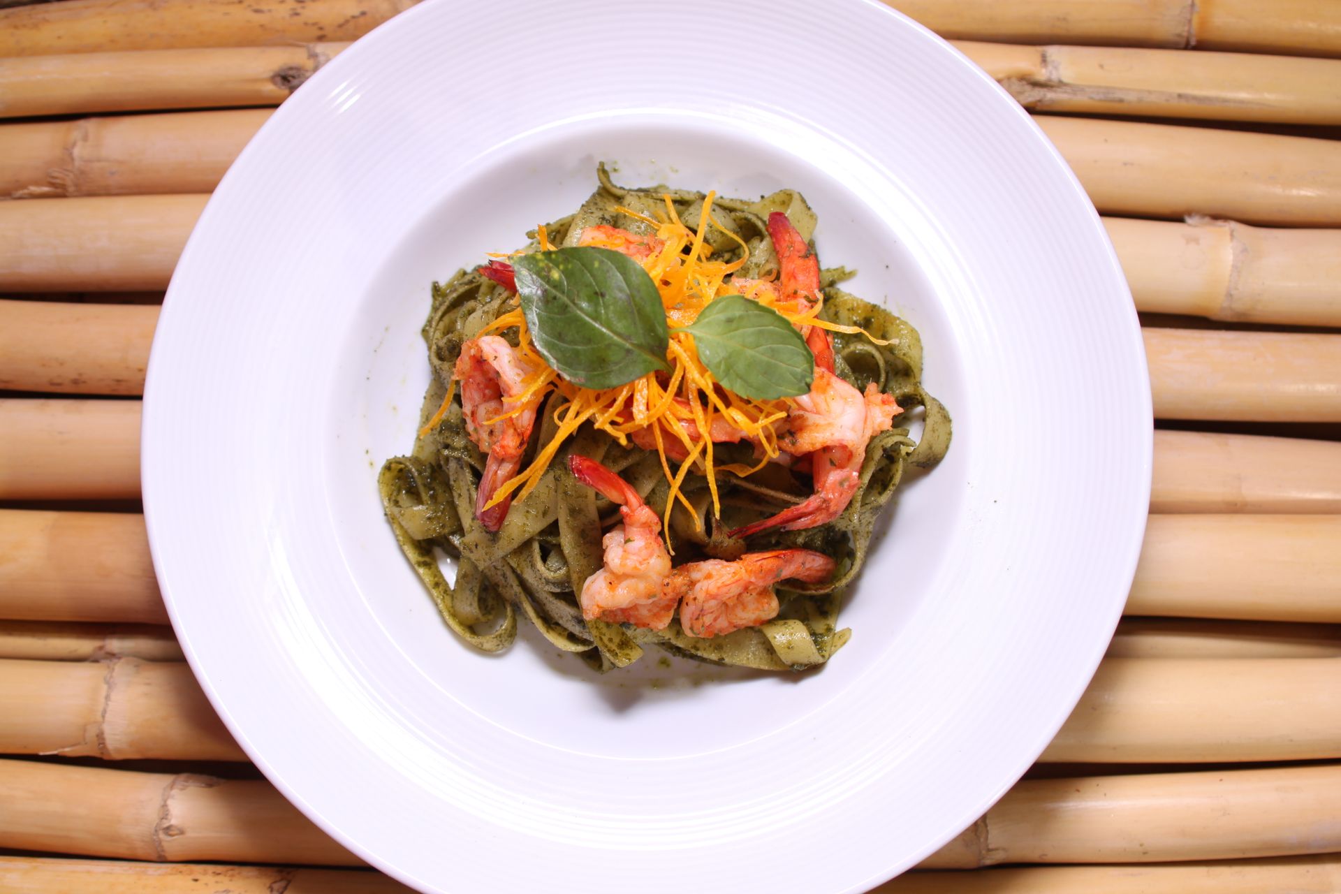 Delicious shrimp pasta dish served on a stylish plate with a bamboo background, showcasing culinary artistry.
