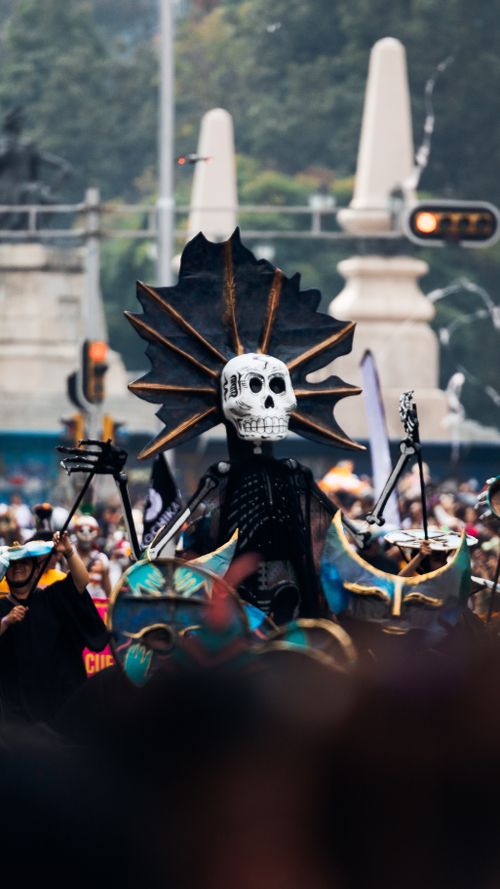 Free Colorful Day of the Dead parade featuring a large skull figure amidst the crowd. Stock Photo